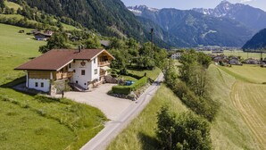 A mountain village with a prominent white building featuring a balcony and a stone foundation.