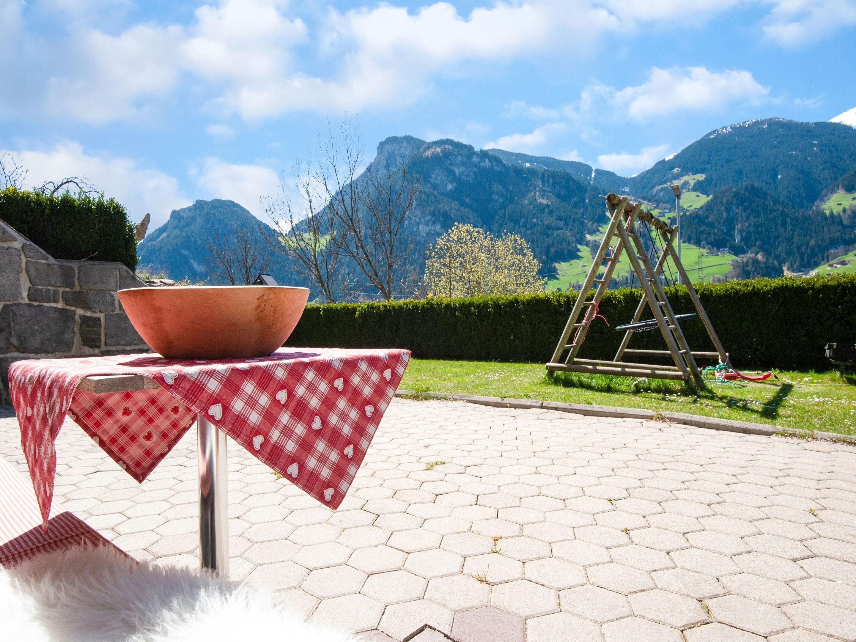A patio with a table set for dining, a large bowl, and a swing set against a mountainous backdrop.