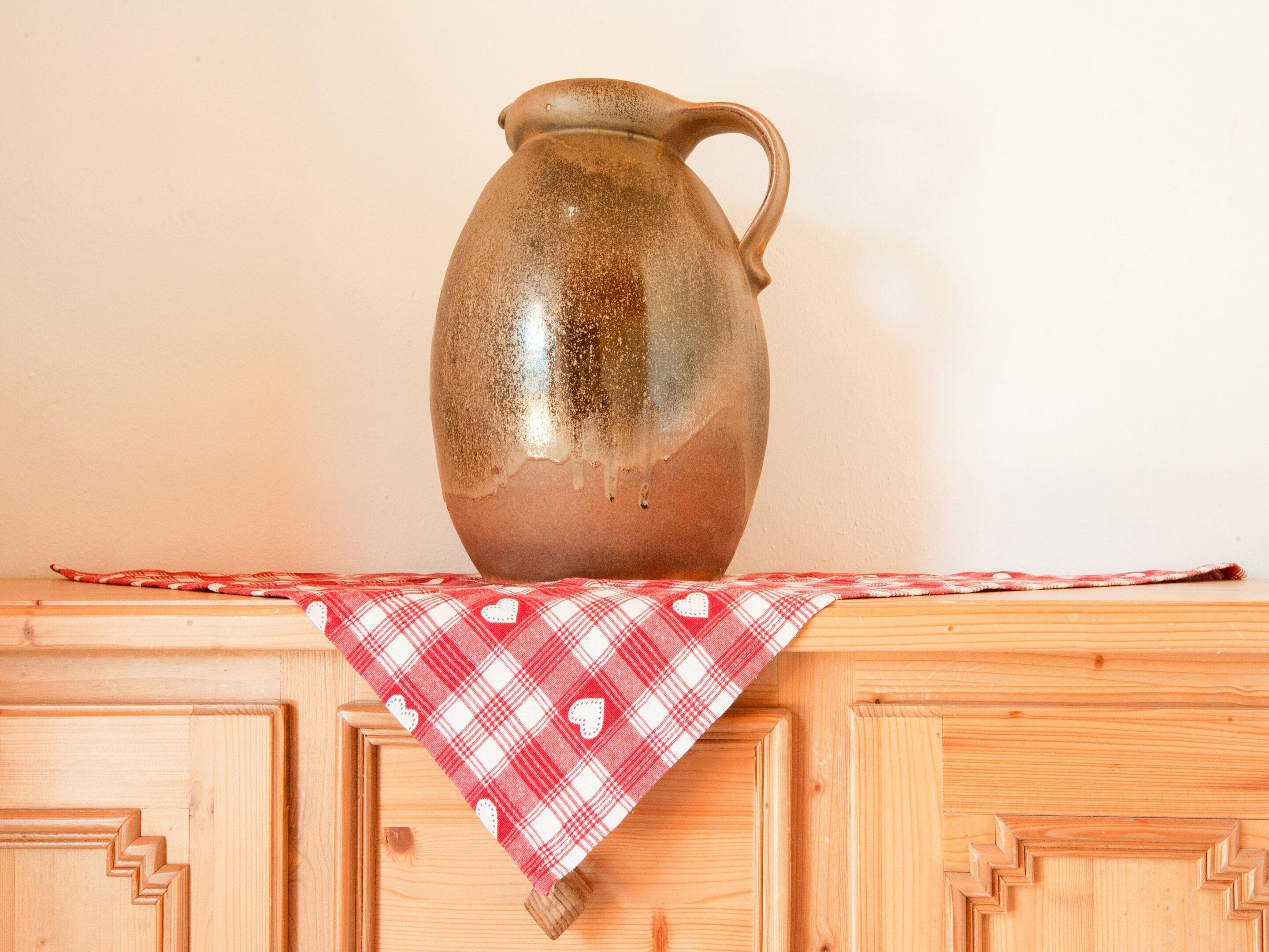 A ceramic pitcher on a wooden cabinet with a red and white checkered cloth.