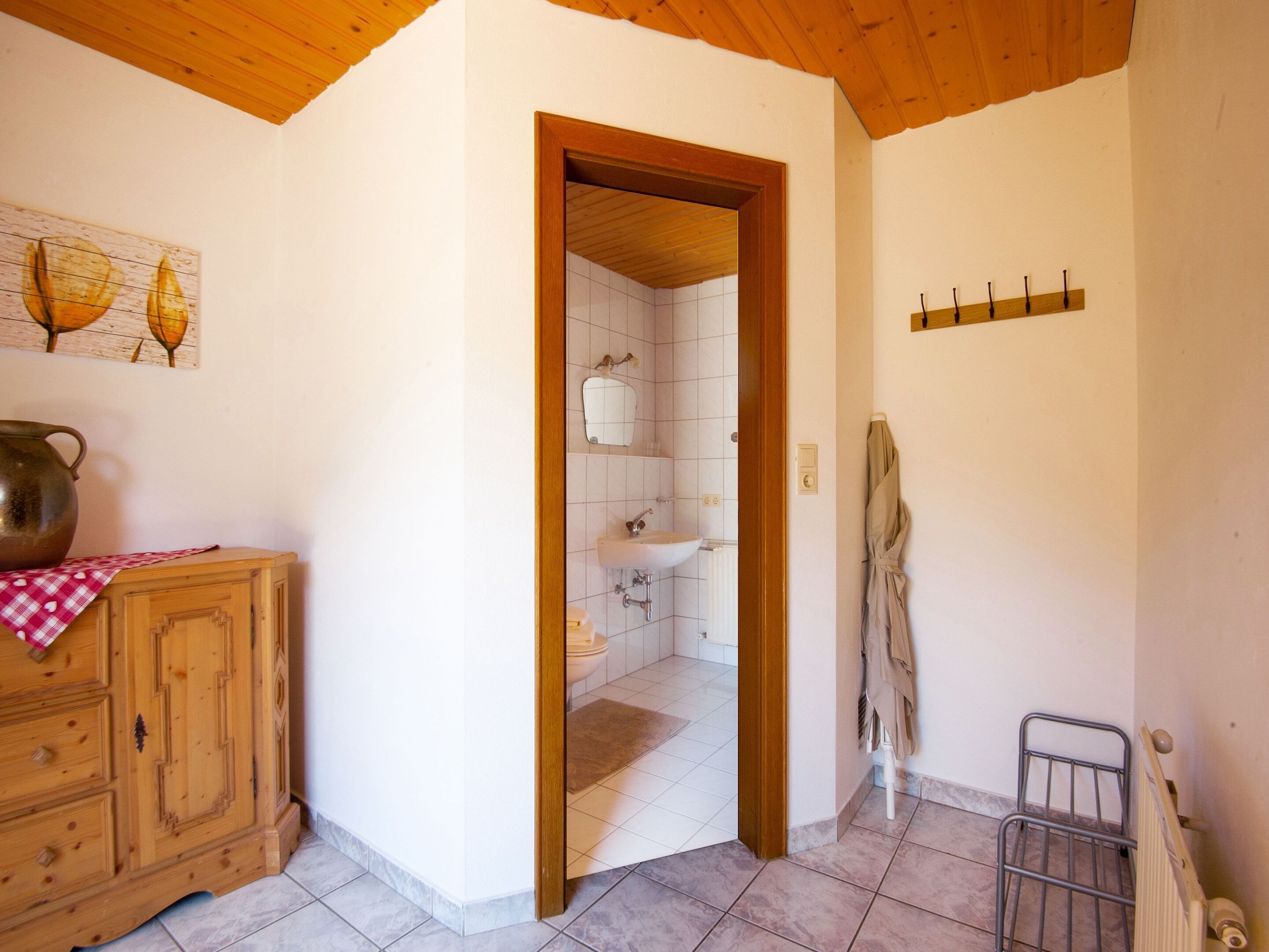 A wooden cabinet with a checkered cloth, a mirror, and a radiator in a room with white walls and wooden ceiling beams.