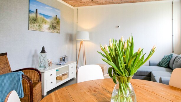 A cozy living room with a wooden table, a white sofa, and a vase of green plants.