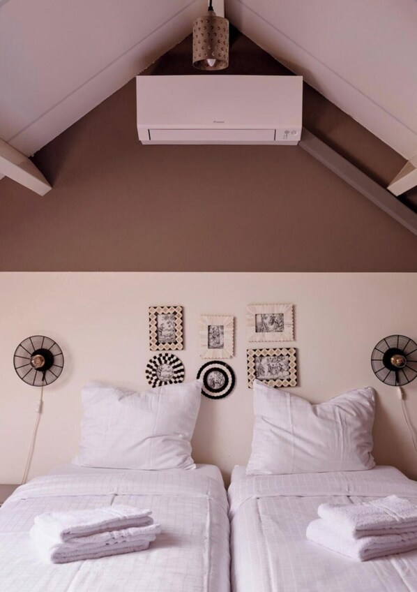 Een slaapkamer met twee bedden, witte beddengoed, een plafondventilator, een airconditioning en wanddecoratie.