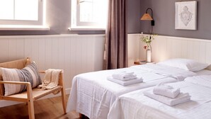 A bedroom with two beds, a chair, a bedside table with a lamp, and a window with curtains. - Holiday Home in Baarlo With Wood-fired Hot Tub (Baarlo)