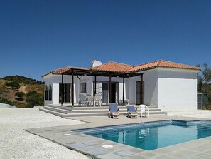 Una casa moderna con piscina, mobiliario exterior y una vista despejada del paisaje circundante.