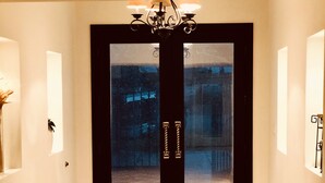 Un pasillo con una puerta oscura, un candelabro y piso de baldosas.