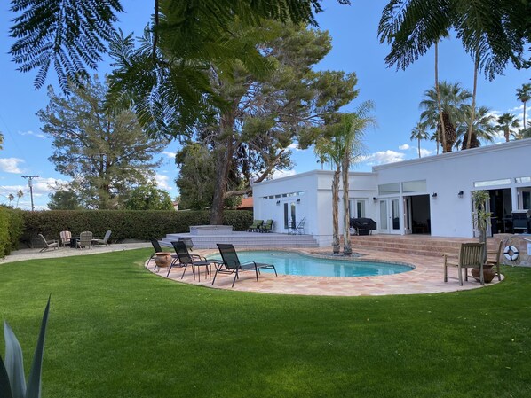 A modern house with a swimming pool, outdoor seating, and a well-maintained lawn.