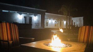 Un espacio al aire libre con mesas y sillas para la noche, una chimenea y un edificio al fondo.