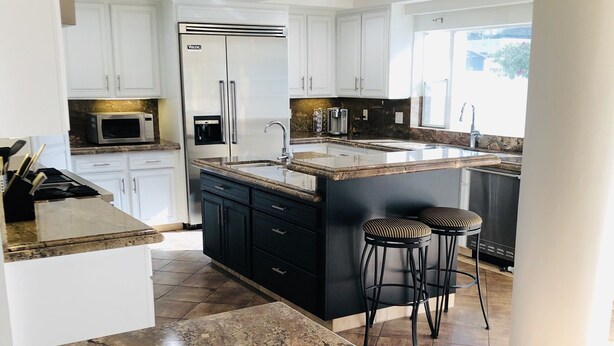 Una cocina moderna con encimeras de granito, electrodomésticos de acero inoxidable y una isla grande con taburetes de bar.