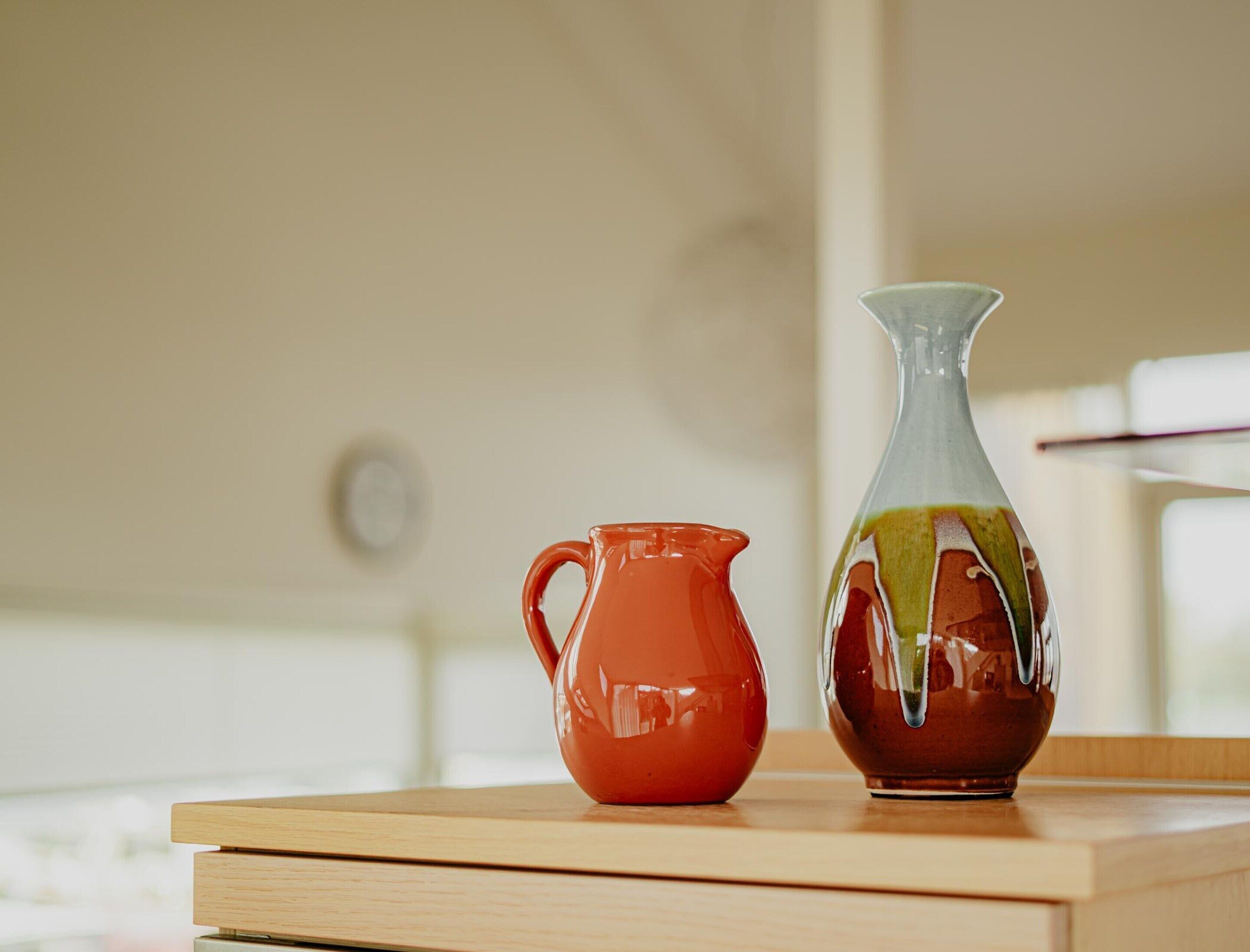 Two ceramic pitchers on a wooden table in a room with a neutral color scheme.