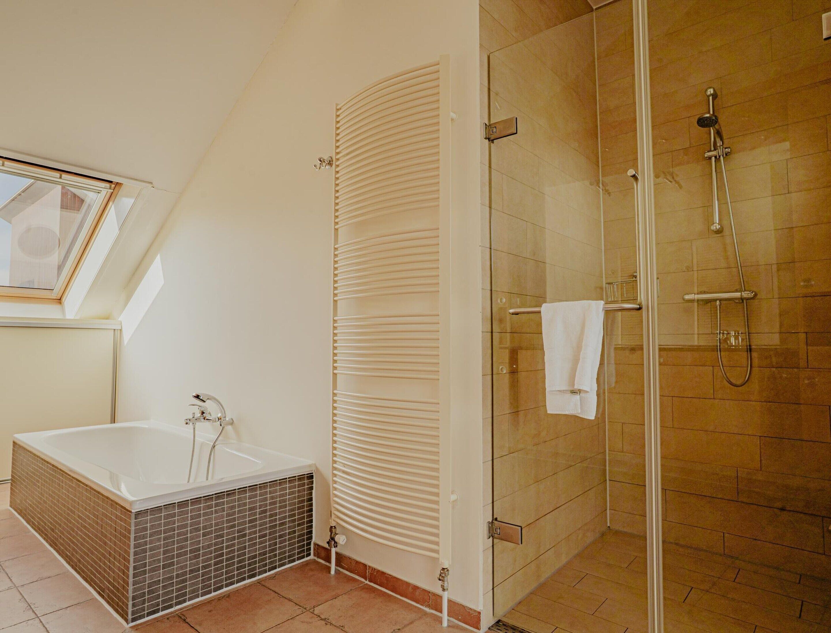 A modern bathroom with a glass shower enclosure, a bathtub with a tiled surround, and a window above the sink.