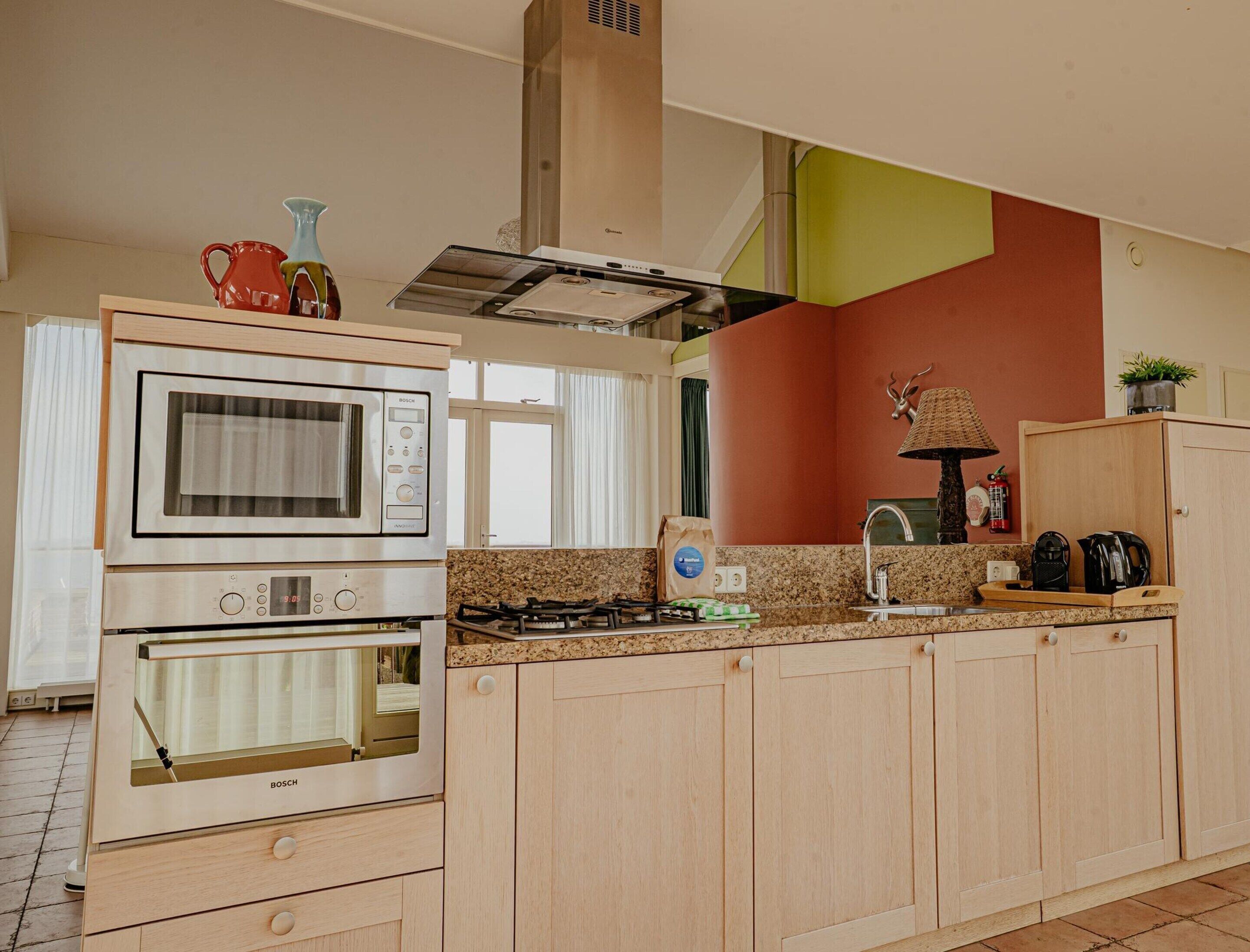A kitchen with a Bosch oven, a gas stove, wooden cabinets, a sink, and a window with curtains.