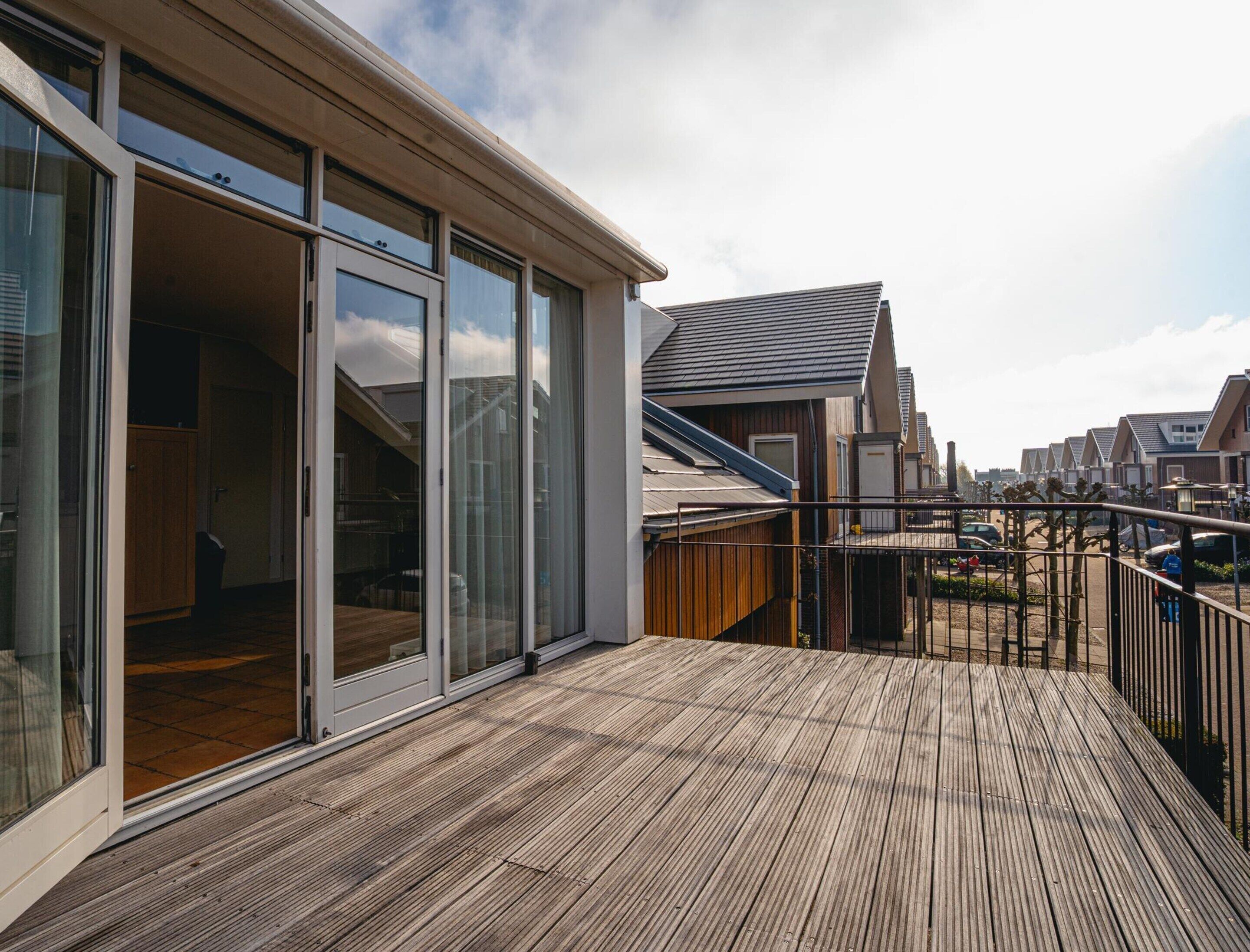 Un moderno edificio residencial con terraza de madera, grandes puertas corredizas de vidrio y vistas a casas vecinas.