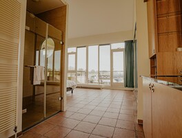 A spacious room with a large sliding glass door leading to a balcony, a bed, and a kitchenette area.