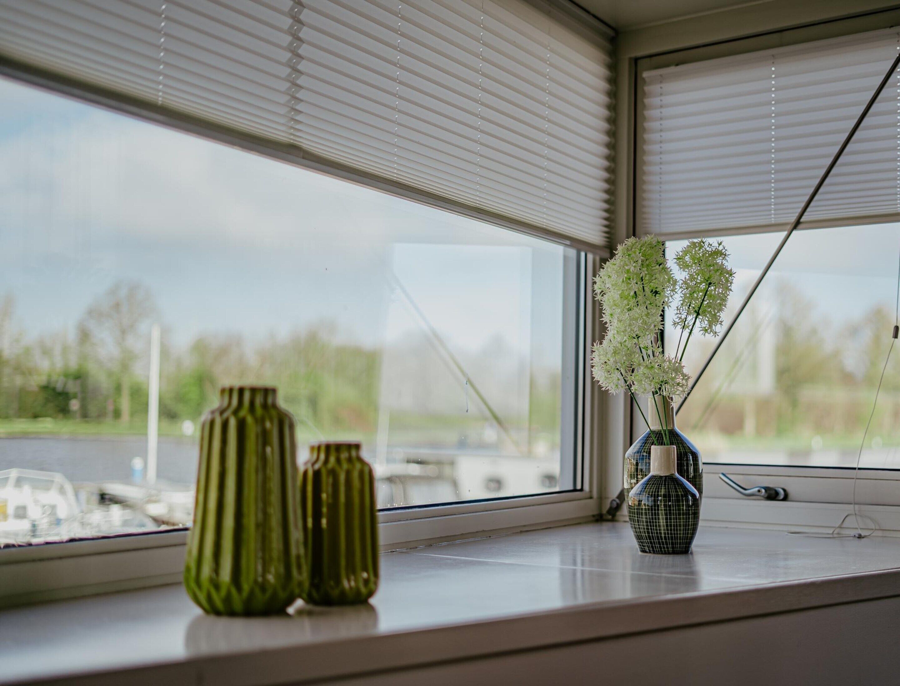 A window with three green vases and a blue vase with white flowers on a ledge.