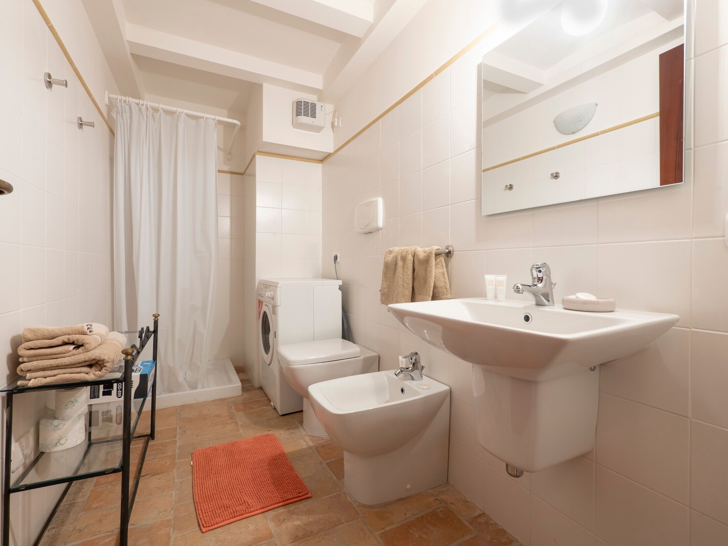 Un bany amb rentamàquines, bidet, rentapousses i una prestatgeria de vidre amb tovellons.