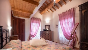 Un dormitorio con una cama, vigas de techo de madera, un aparador y un cuadro sobre caballete.
