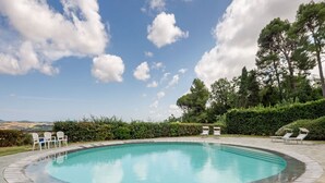 Una piscina circular con borde de piedra, rodeada de sillas de descanso y vistas al campo.