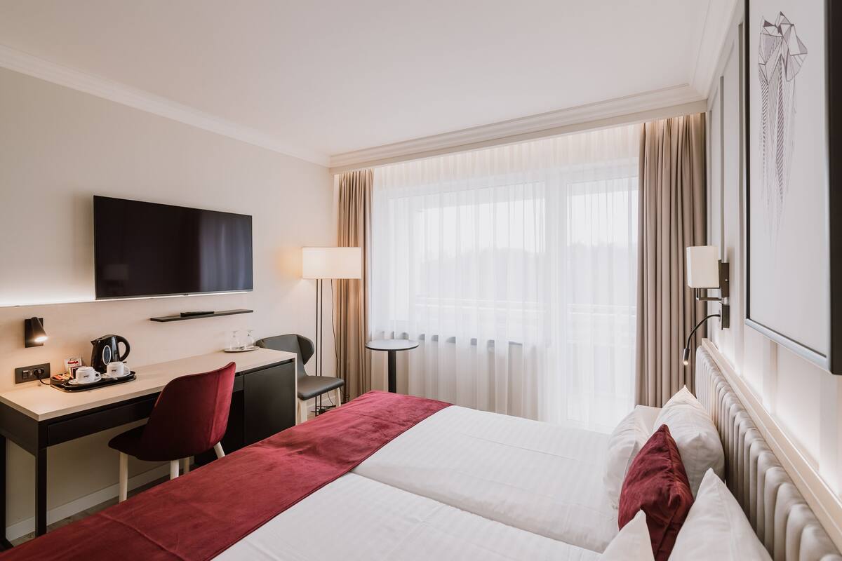 A hotel room with a bed, a desk, a chair, a TV, and a window with curtains.