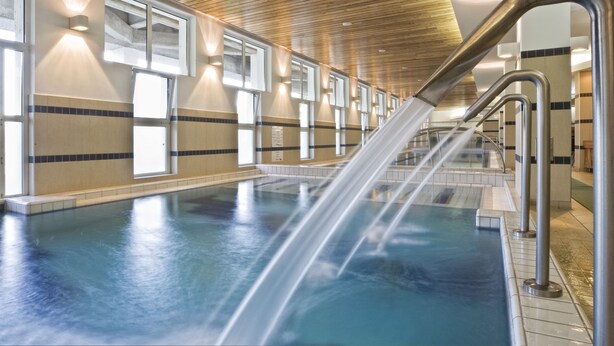 A swimming pool with a water feature, wooden ceiling, and tiled walls. - Ensana Sovata (Sovata)