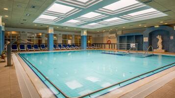 Ein Hallenbad mit klarem, blauem Wasser, umgeben von blauen Liegestühlen und einem gefliesten Boden.