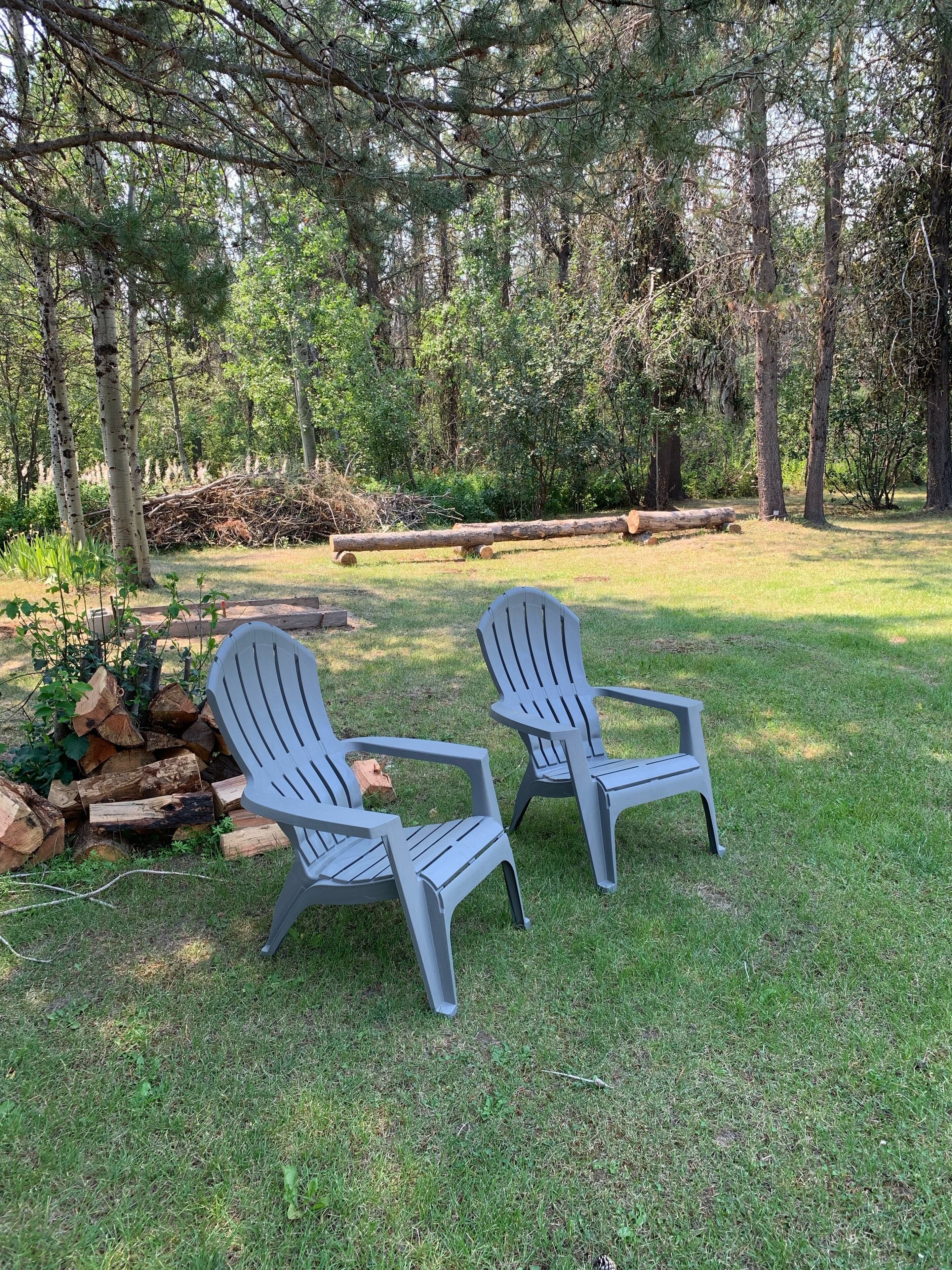 Dos sillas Adirondack en un espacio exterior con césped y árboles al fondo.