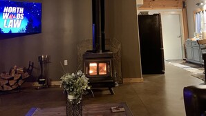 Un acogedor interior de cabaña con chimenea de piedra, vigas de madera, televisor y comedor con un jarrón de flores.