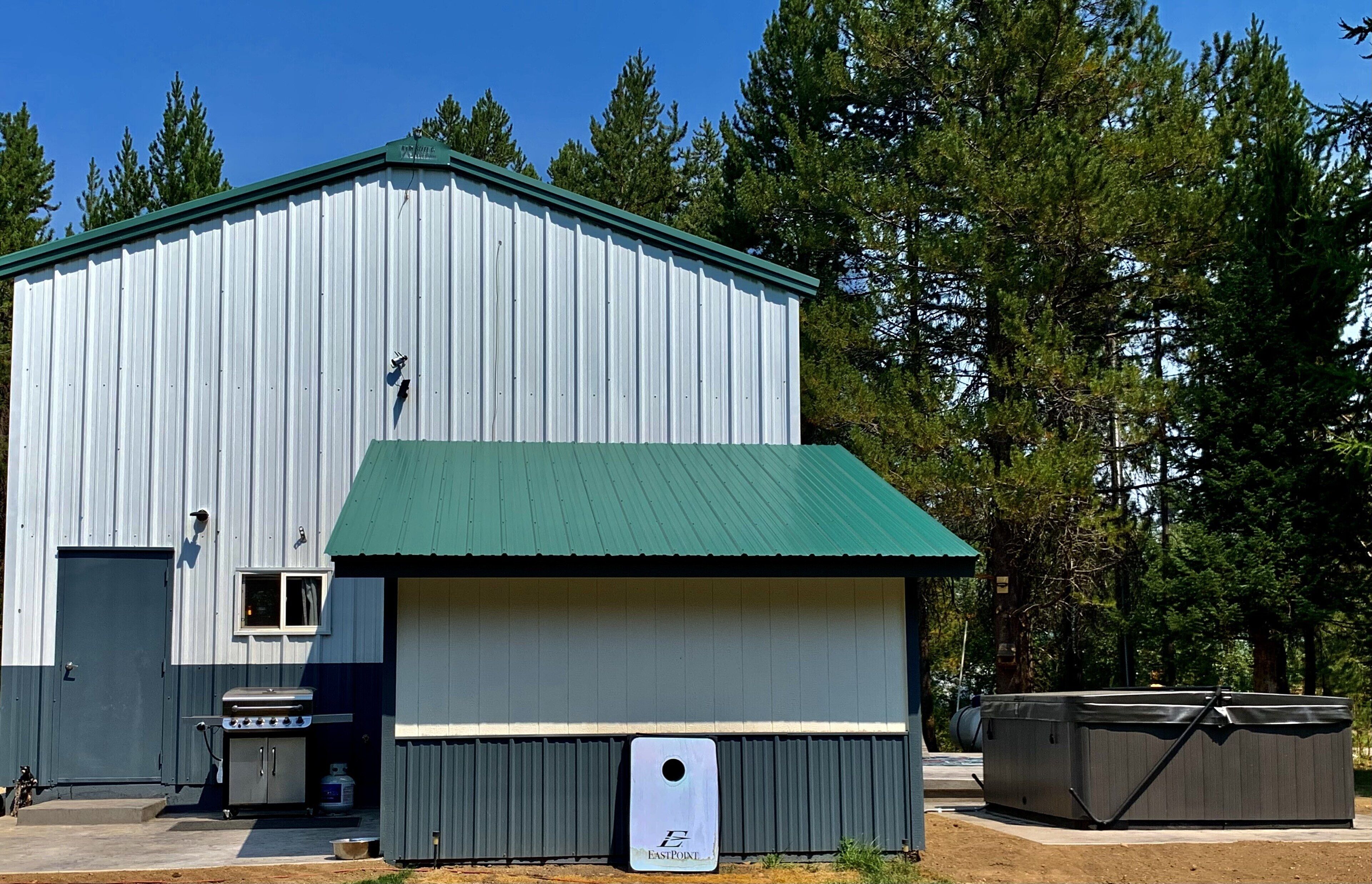 A large metal building with a green roof, a barbecue grill, and a hot tub outside.