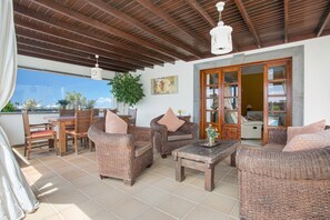 A covered patio with wicker furniture, a wooden table, and a view of the outside. - Holiday Villa Capricho with Sea & Mountain View & Pool (Lanzarote)