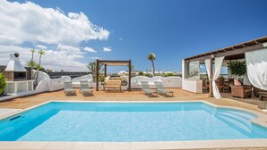 A rooftop pool with lounge chairs, a wooden pergola, and a view of the city. - Holiday Villa Capricho with Sea & Mountain View & Pool (Lanzarote)