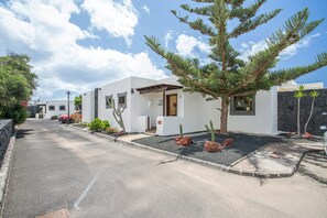 A modern building with a white facade, a stone wall, and a tree in the foreground. - Holiday Villa Capricho with Sea & Mountain View & Pool (Lanzarote)
