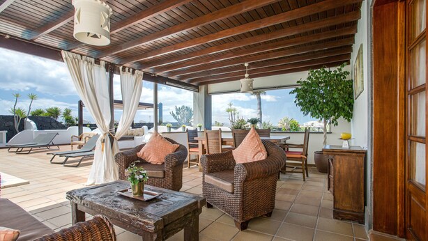 A covered outdoor seating area with wicker furniture, a wooden table, and a view of the sky. - Holiday Villa Capricho with Sea & Mountain View & Pool (Lanzarote)