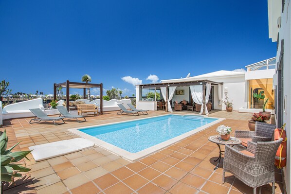 A pool area with lounge chairs, a pergola, and a covered seating area. - Holiday Villa Capricho with Sea & Mountain View & Pool (Lanzarote)