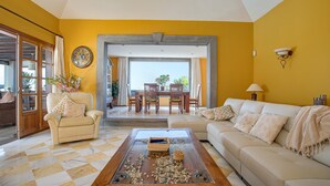 A living room with a checkered floor, a sofa, a coffee table, and a dining area with chairs and a table. - Holiday Villa Capricho with Sea & Mountain View & Pool (Lanzarote)