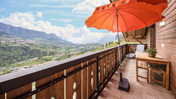Ein Holzbalkon mit Tisch, Stuhl und Sonnenschirm.