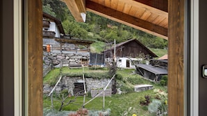 Ein Blick auf ein traditionelles Holzhaus mit Stein Fundament, umgeben von einem gepflegten Garten und einer Hügelkulisse.