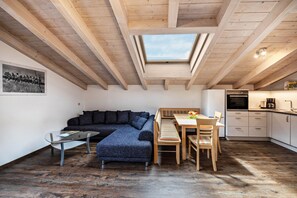Avoin, loft-tyylinen huone, jossa on kattovalokuvio, sohva, ruokapöytä ja keittiötila.