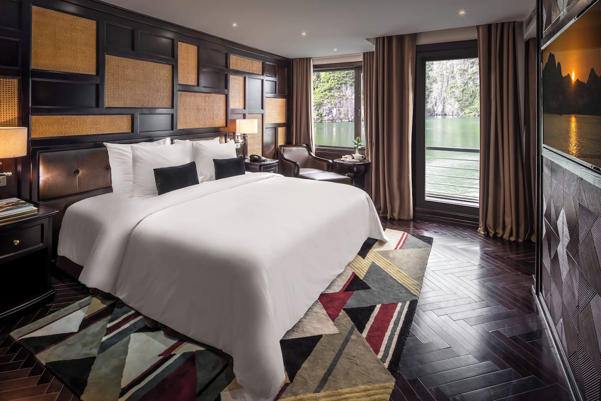 A hotel room with a large bed, a view of the water, and a TV on the wall.