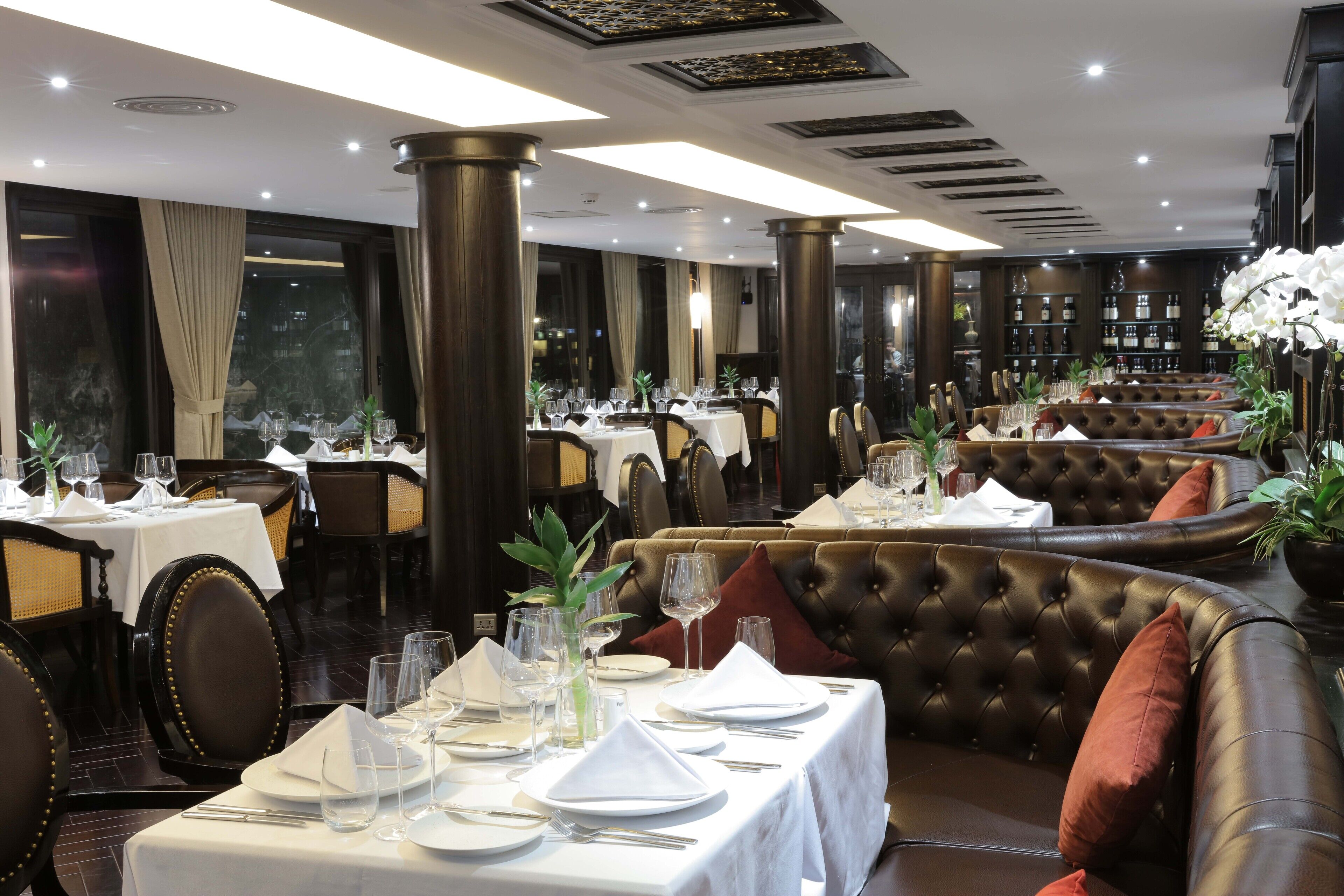 A restaurant with tables set for dining, featuring leather booths and a bar area with wine bottles.