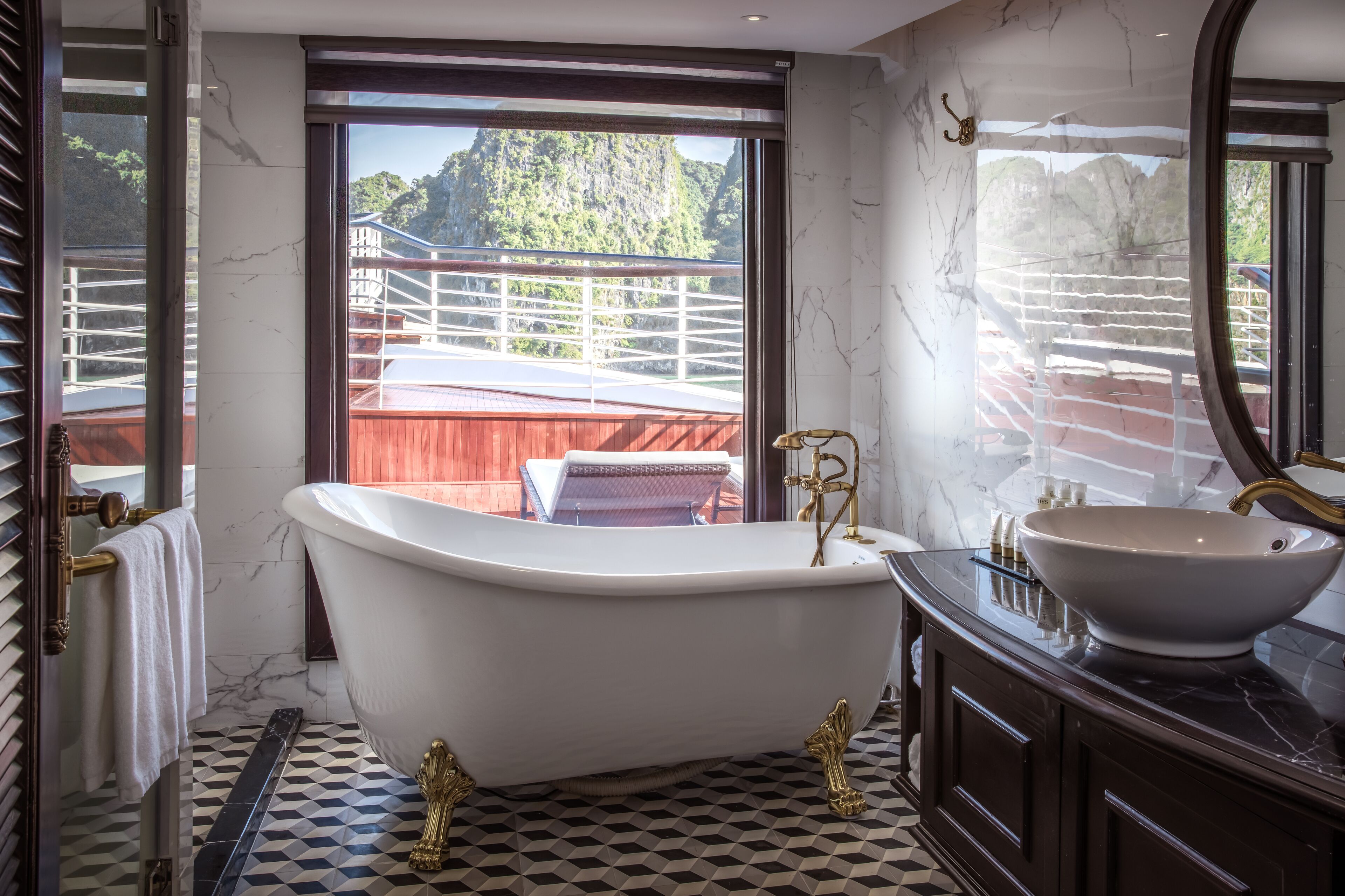 Ein Badezimmer mit einer freistehenden Badewanne, einem großen Spiegel und Blick auf einen Balkon mit Geländer.
