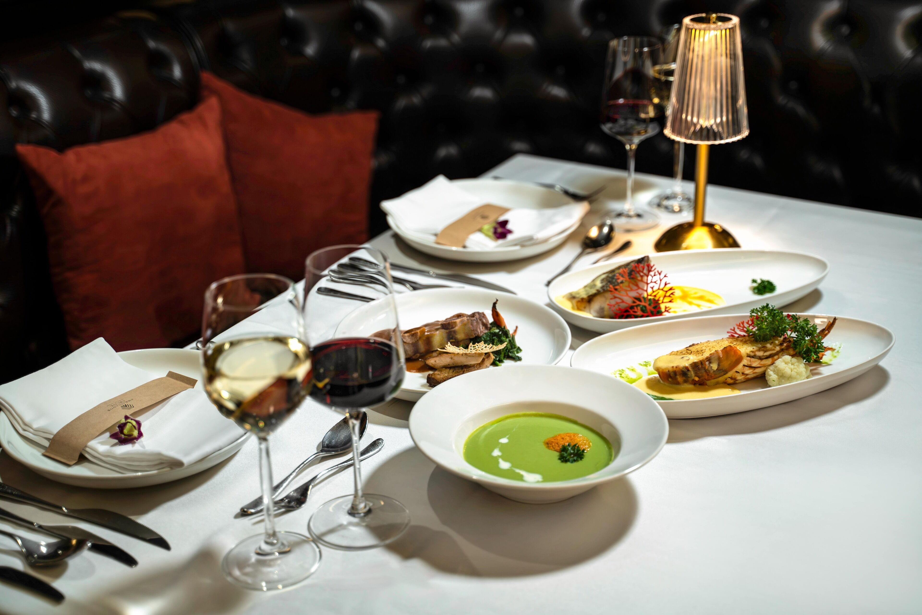 A dining table set with various dishes, wine glasses, and a lamp.
