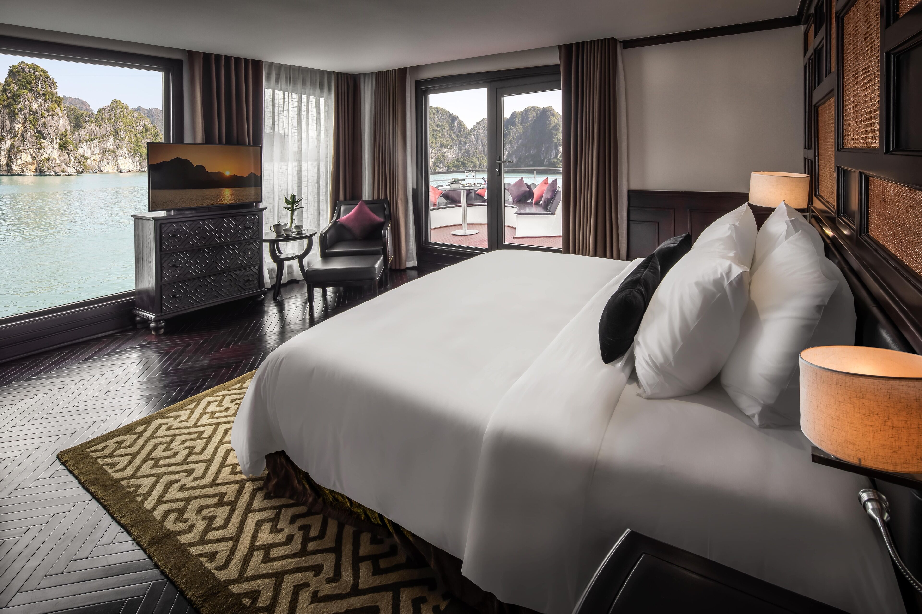 A hotel room with a large bed, a TV, a desk, and a view of a body of water.