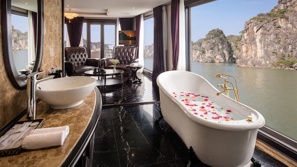 A luxurious bathroom with a large bathtub, a sink, and a seating area with chairs. - Ambassador Cruise Halong Bay (Bai Chay)