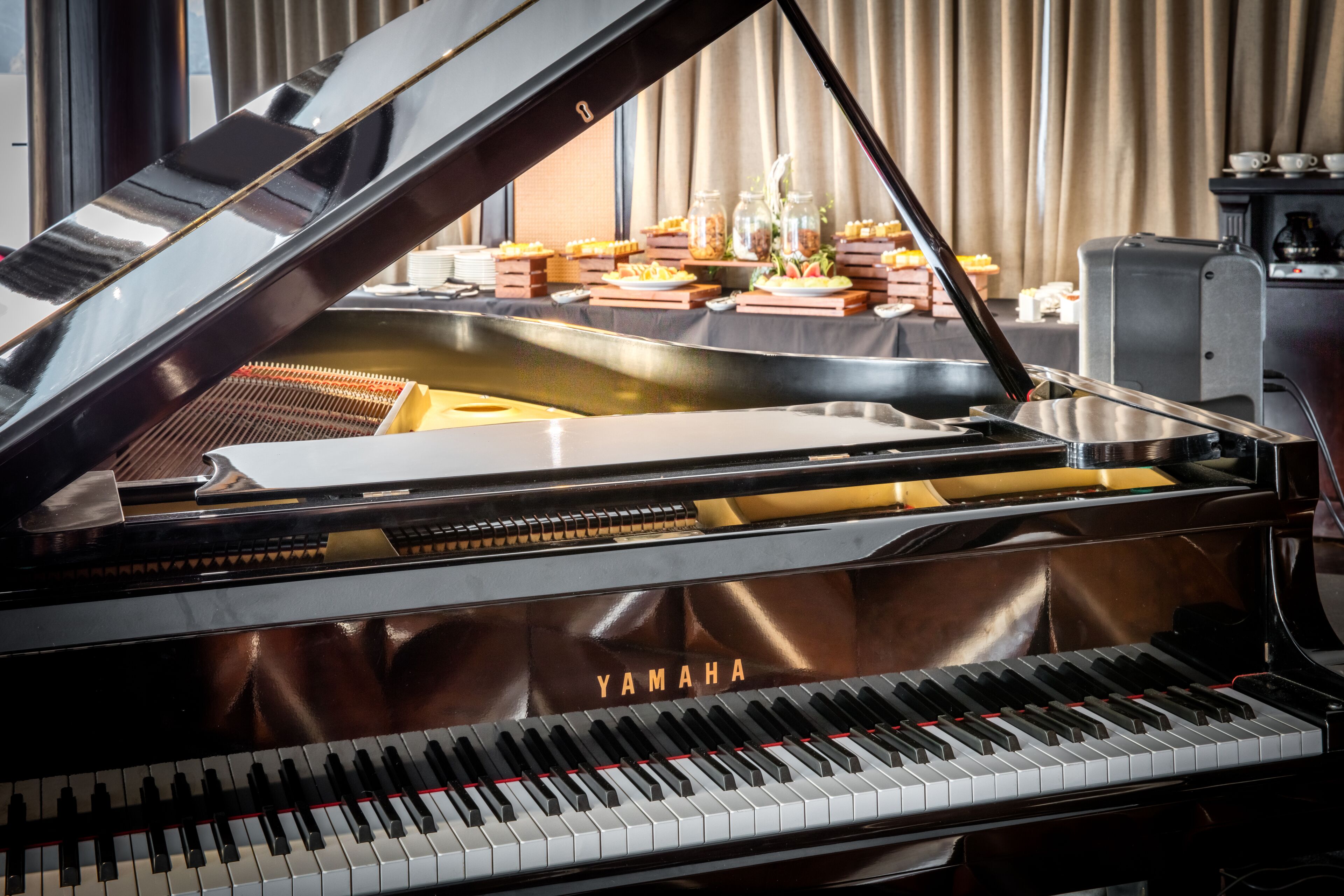 A grand piano with a Yamaha logo, a buffet table with various dishes, and a coffee machine in the background.