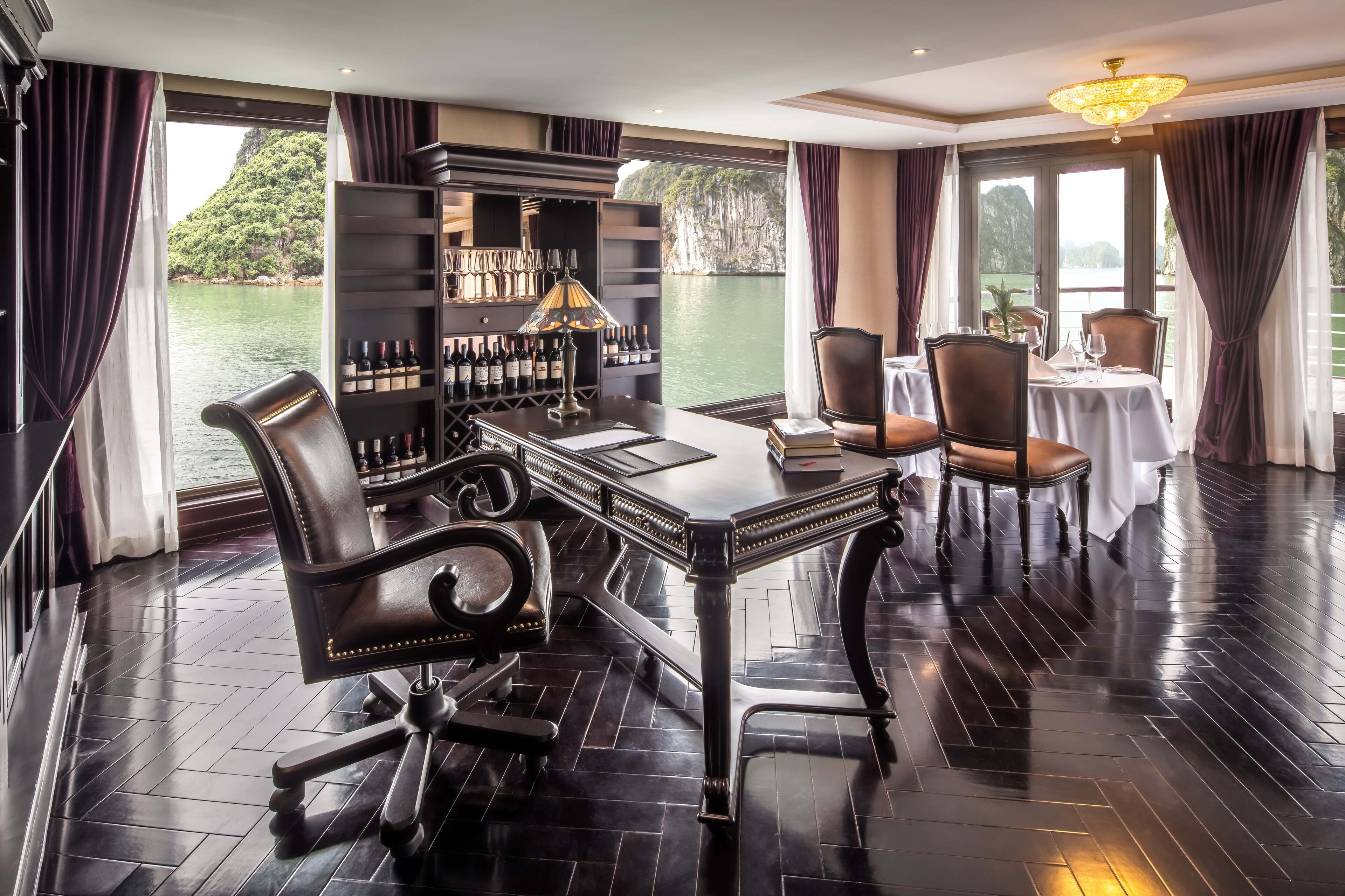 A luxurious room with a polished wooden floor, a bar area with a wine rack, and a dining table set for two.