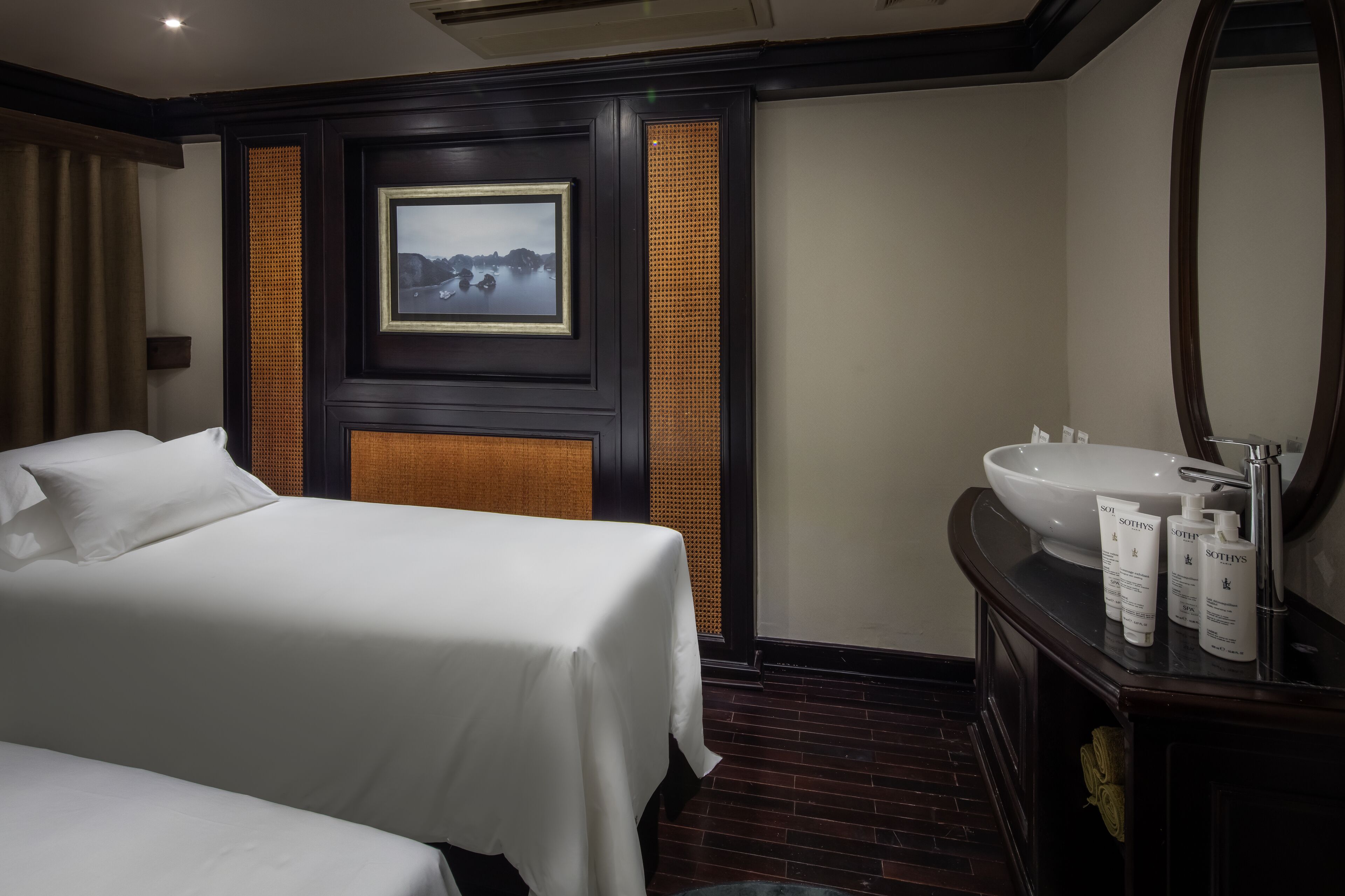 A hotel room with a bed, a large mirror, a sink with toiletries, and a framed picture on the wall.