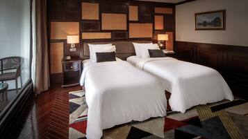 A hotel room with two beds, a wooden floor, a patterned rug, and a wall with a geometric design.