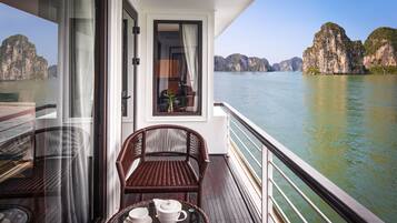 Un balcon agrémenté de meubles en osier et d’une table où sont disposés des tasses à thé et une théière, offrant une vue sur une étendue d’eau paisible et des falaises calcaires.