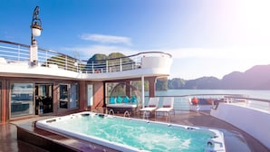 A luxurious outdoor hot tub area with a wooden deck, lounge chairs, and a seating area with cushions. - Ambassador Cruise Halong Bay (Bai Chay)