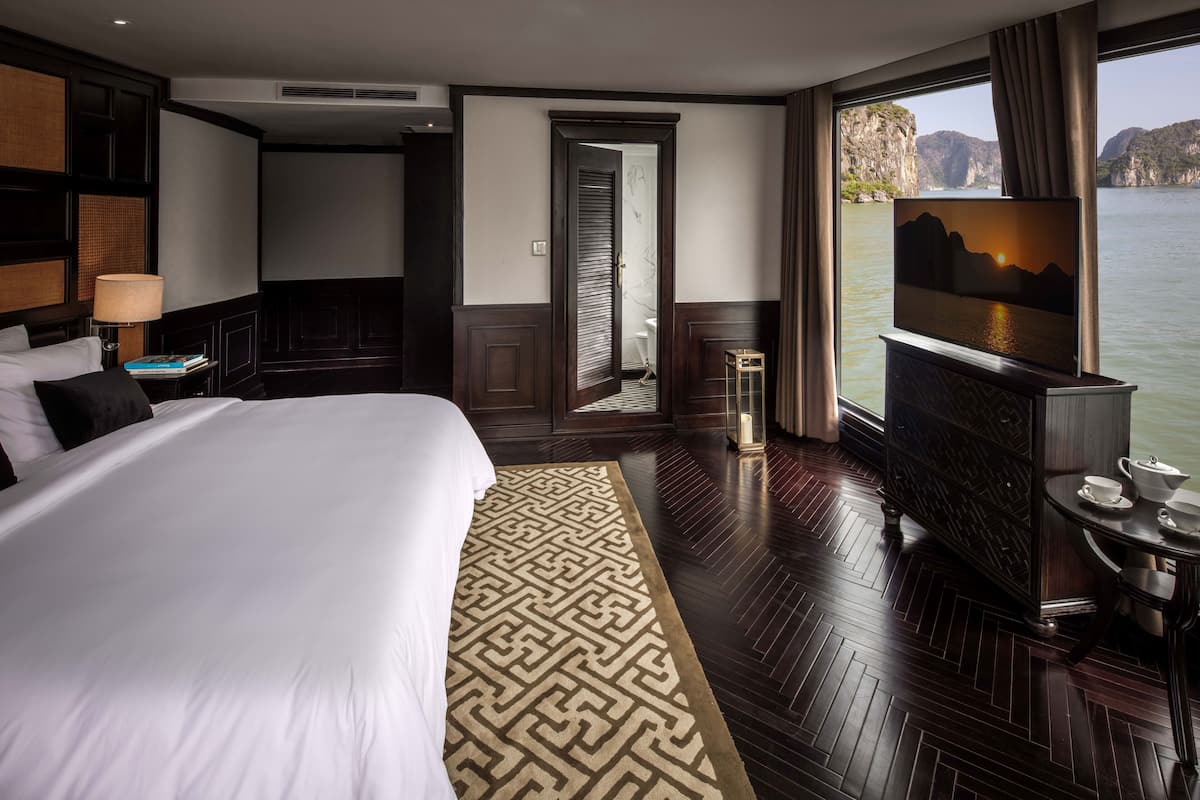 A hotel room with a large bed, a television, a small table with a cup and saucer, and a view of a body of water.