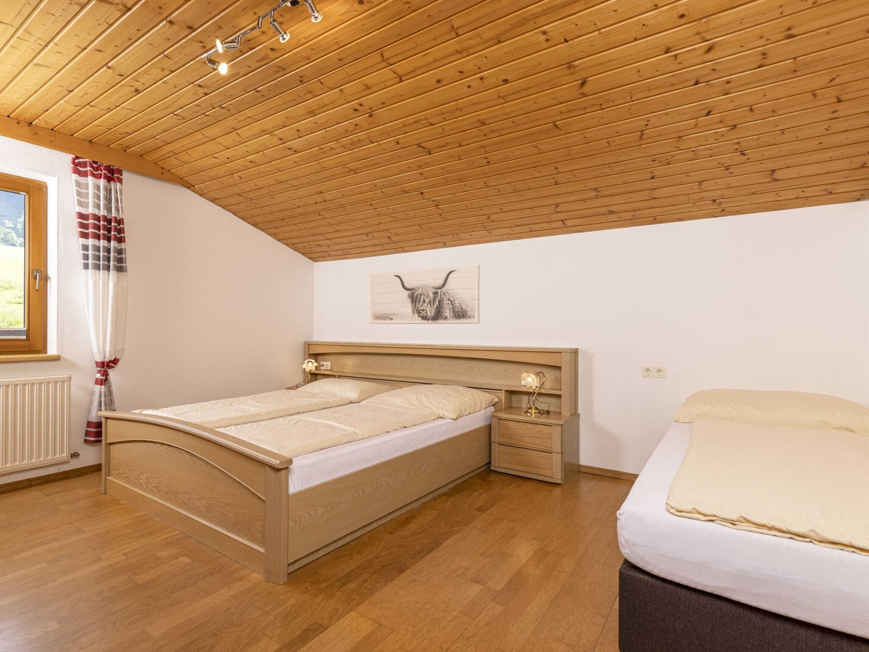 Ein Schlafzimmer mit Holzboden, einem Bett mit Kopfteil, einem Nachttisch mit Lampe und einem Fenster mit Vorhängen.